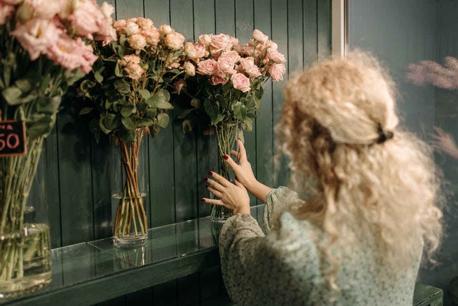 An outdoor display of fresh flower bouquets arranged on a wooden cart and various buckets, featuring a vibrant assortment of blooms including pink lilies, orange roses, red carnations, purple irises, 